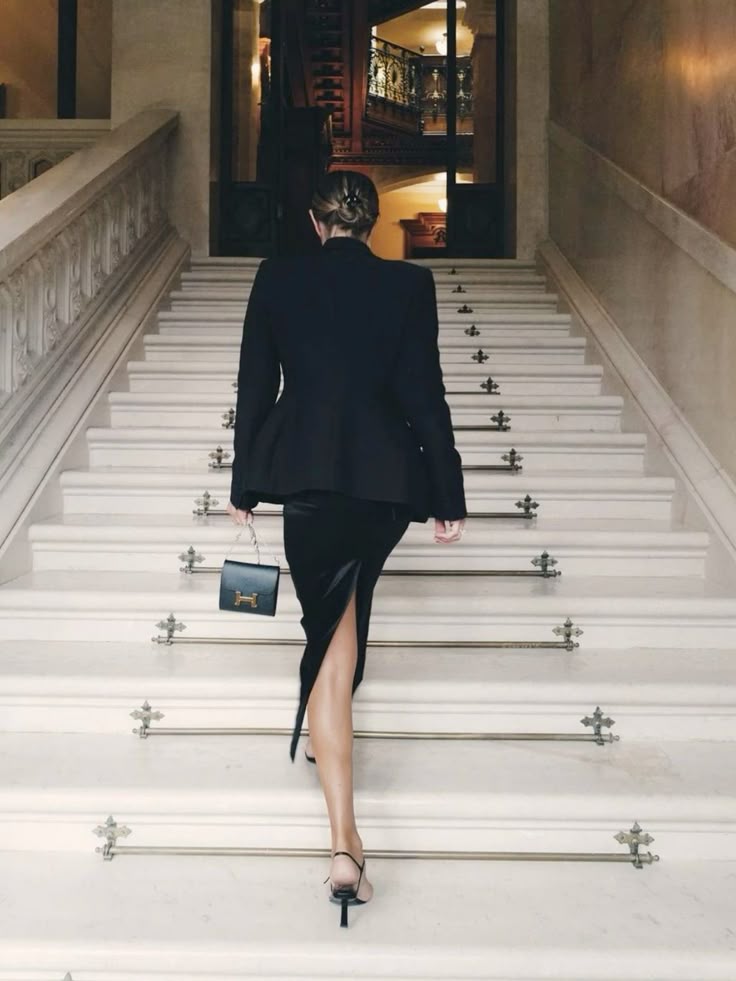 Bella in black, walking up a grand marble staircase — public again